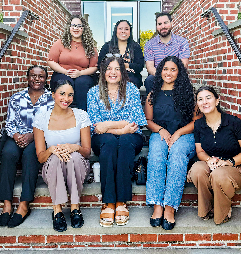 A group of male and female students sit on steps outside of a brick building.